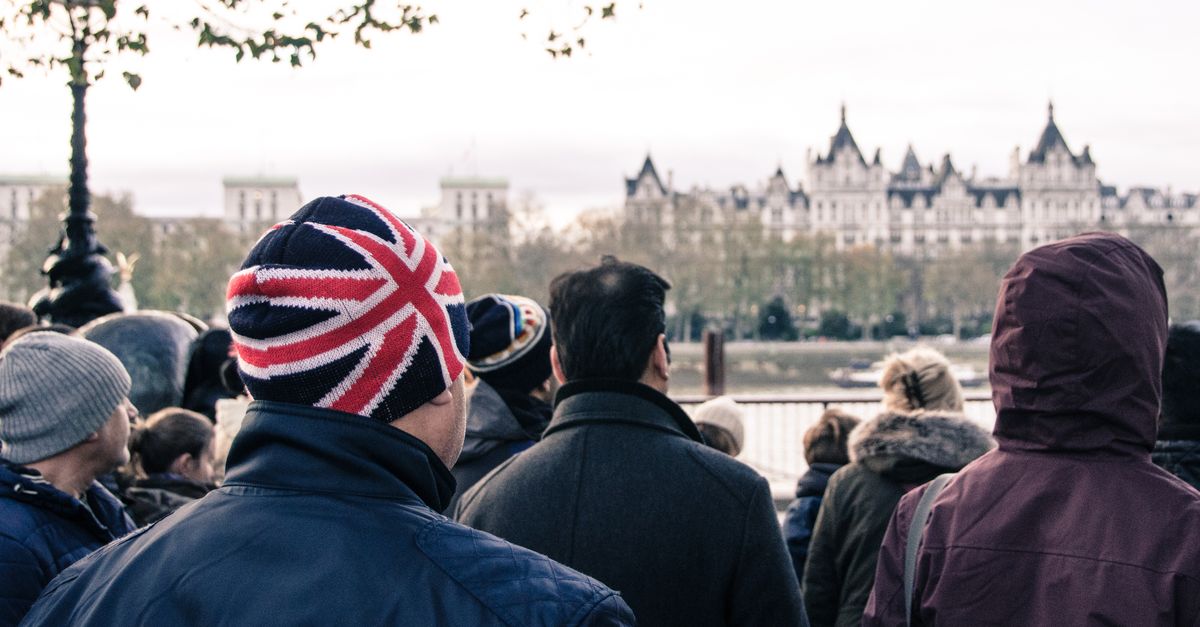 A crowd in London faces iconic architecture. Prominent British Union Jack hat in focus.