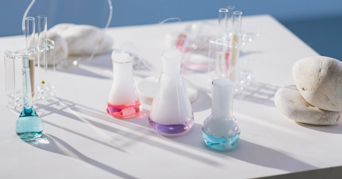 Vibrant chemical liquids in flasks and test tubes on a sunny white table with stones.