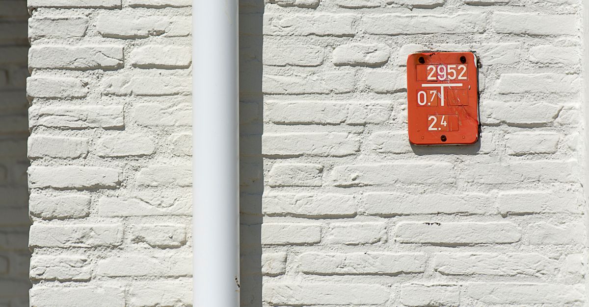 Close-up of a white brick wall featuring a red numbered sign with a white gutter pipe.
