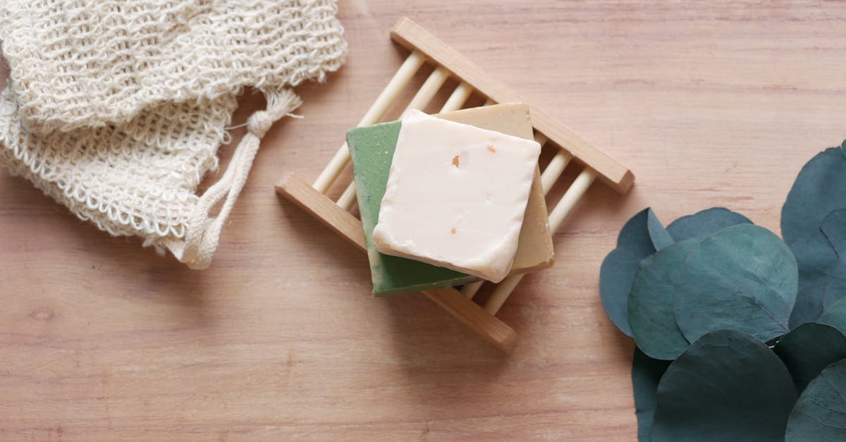 Top view of handcrafted soap bars on bamboo dish with green leaves, featuring a rustic wooden background.