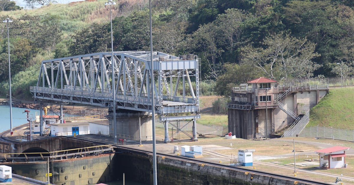 Steel bridge spanning a canal lock amidst lush greenery, captured from a high angle.