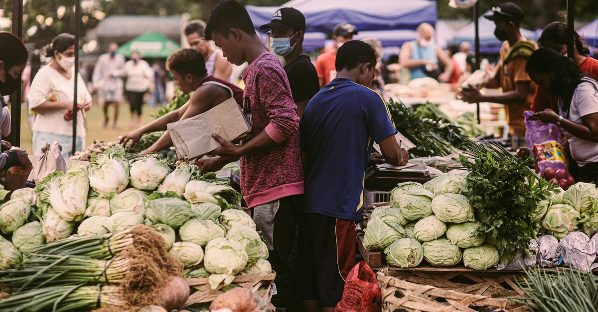 Vibrant farmers market scene with diverse people and fresh vegetables on a sunny day.