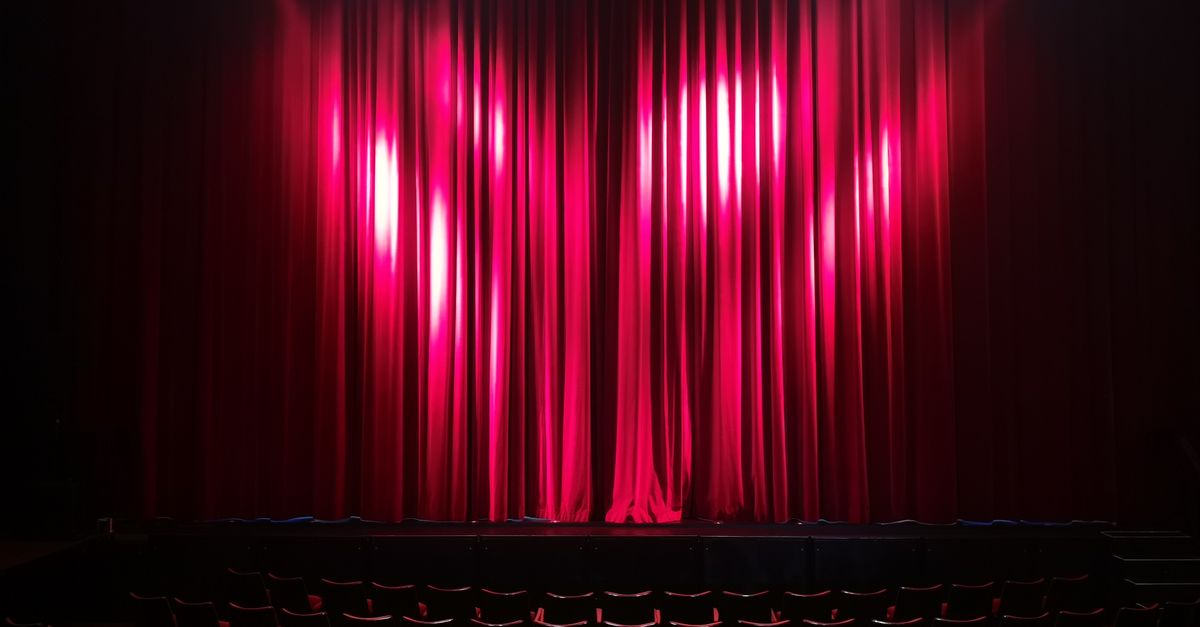 Empty theater stage with red curtains and seating, ready for a performance.