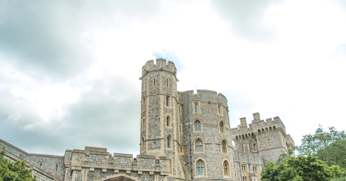View of Windsor Castle's stone architecture with cloudy sky backdrop and lush greenery.