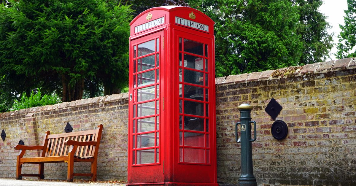 A vintage red telephone booth beside a brick wall, symbolizing British culture.