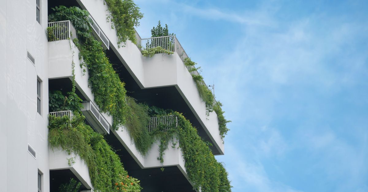 A residential building showcasing lush vertical gardens on multiple balconies against a clear blue sky.