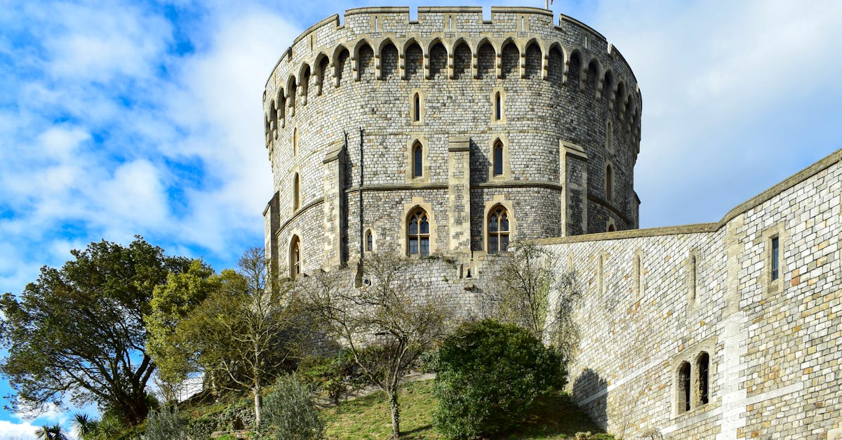 View of Windsor Castle's iconic Round Tower against a clear blue sky, surrounded by greenery.