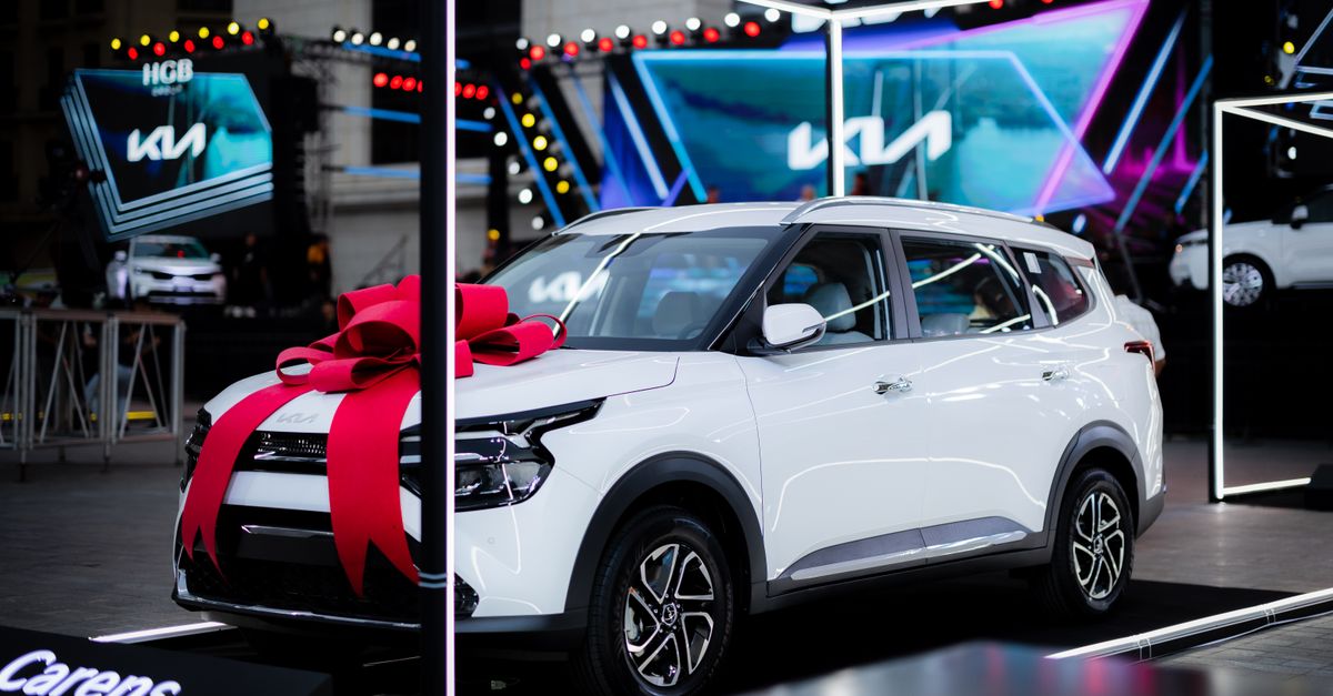 White car with a red bow on display at an automotive exhibition under bright lights.
