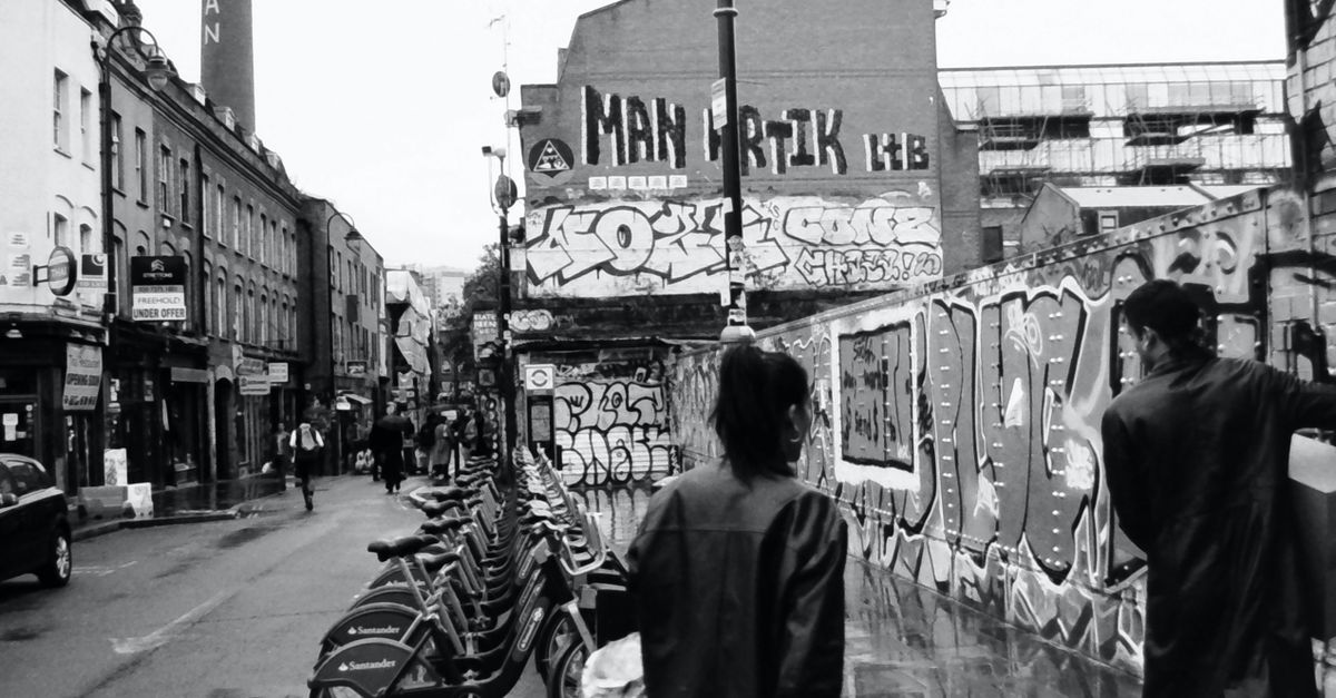 Monochrome street scene with graffiti and pedestrians on Brick Lane, London.