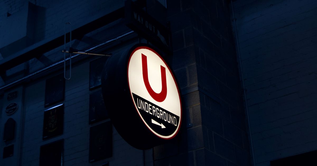 Close-up of a glowing 'Underground' sign in a dark urban setting.