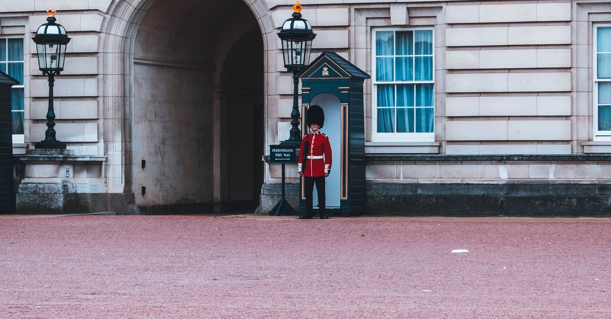 A guard in traditional red uniform stands at Buckingham Palace, London, United Kingdom.