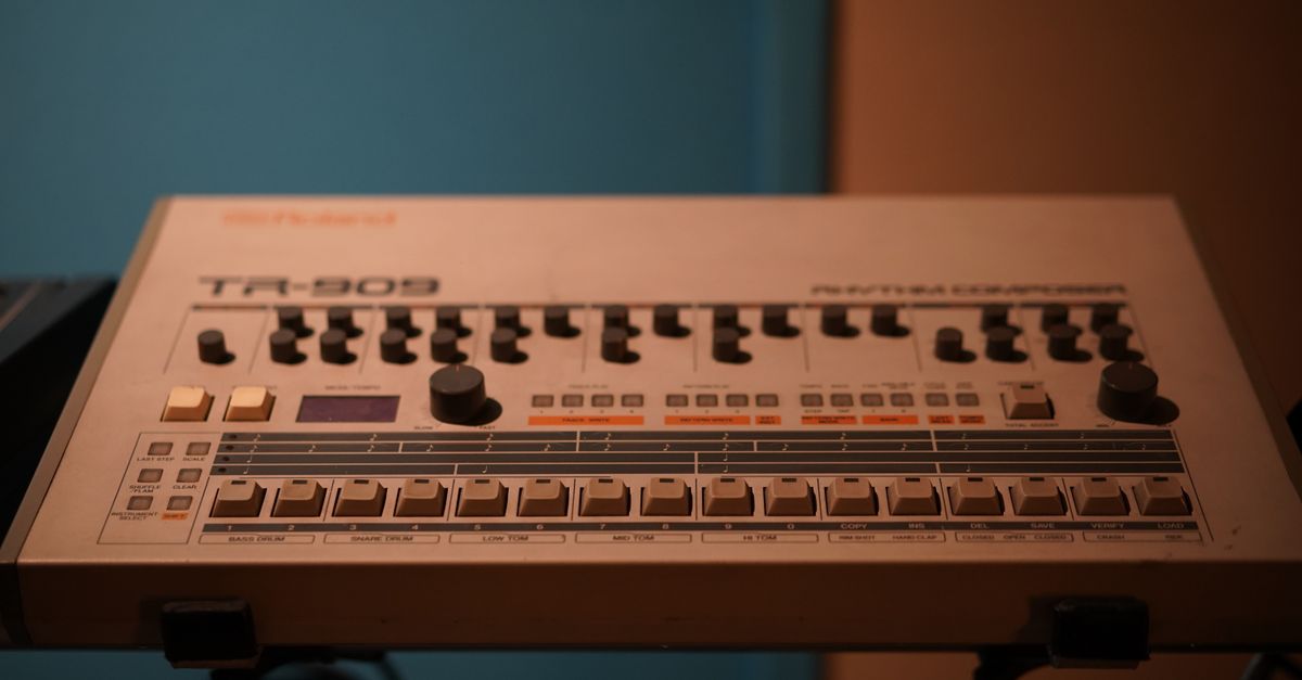Close-up of a classic Roland TR-909 drum machine in a studio setting.