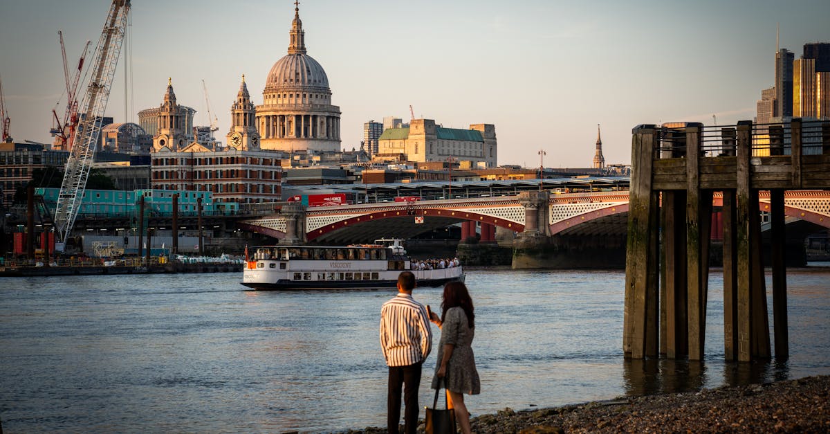 A couple standing by the Thames in London, overlooking St Paul's Cathedral during sunset with cityscape backdrop.