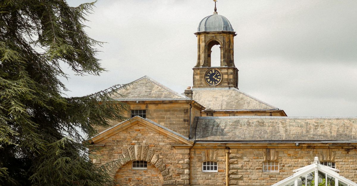 Stone building with clock tower and trees against an overcast sky.
