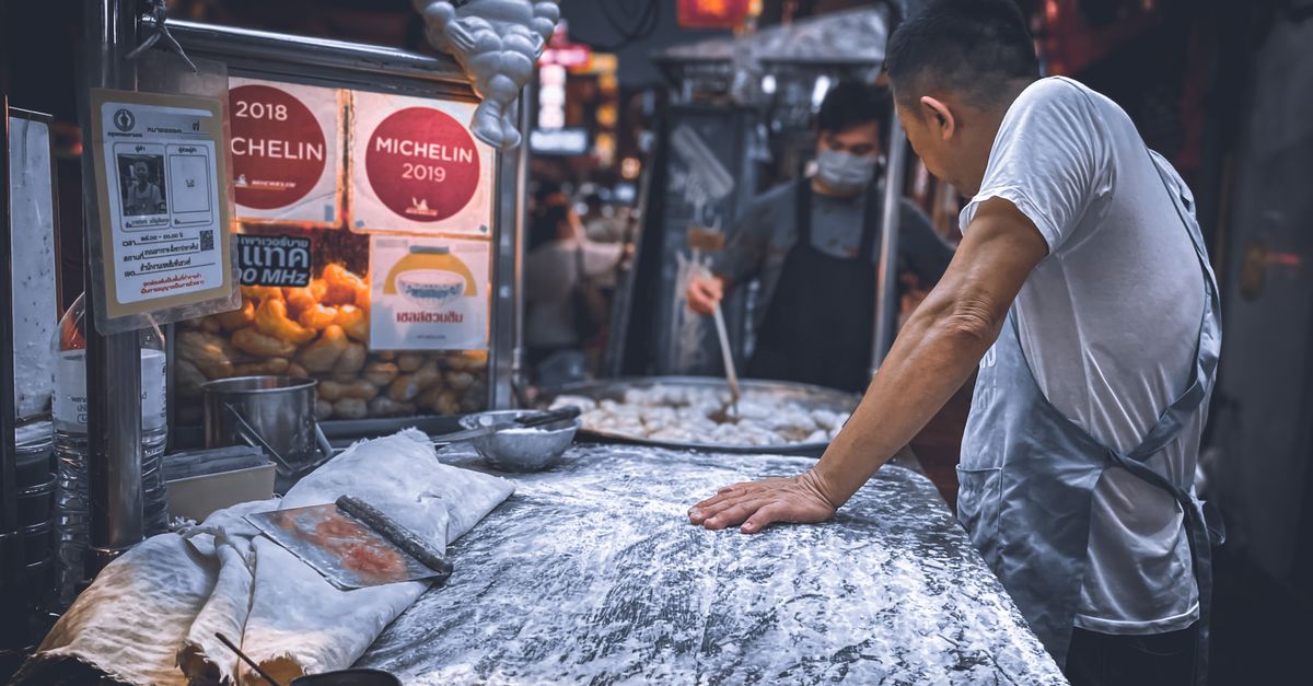 Street food vendor preparing dough in a bustling night market in Bangkok, Thailand.