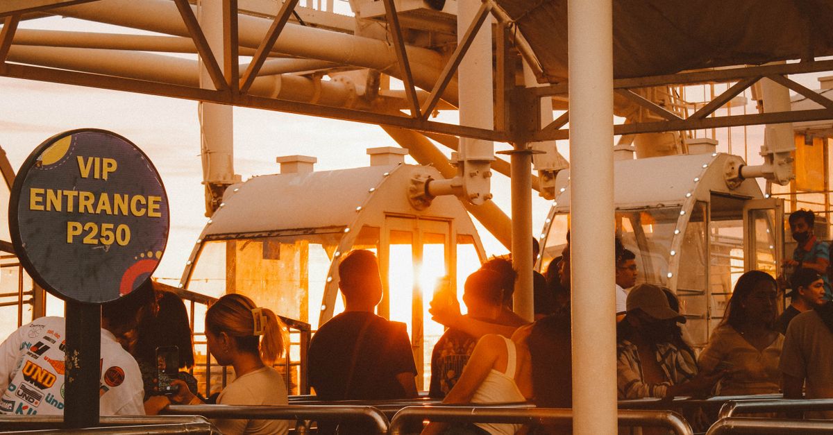 Tourists queuing for a ferris wheel ride at sunset with VIP entrance sign.