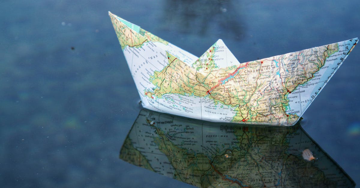 A paper boat folded from a map floats on water, creating a unique reflection.