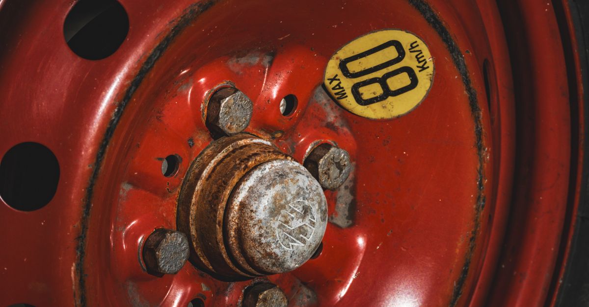 Detailed view of a rusty red spare car wheel with an '80 KM/H' max speed warning label.