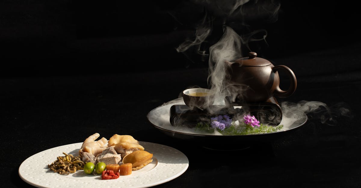 A steaming teapot with Asian dishes on black background, showcasing elegant food photography.
