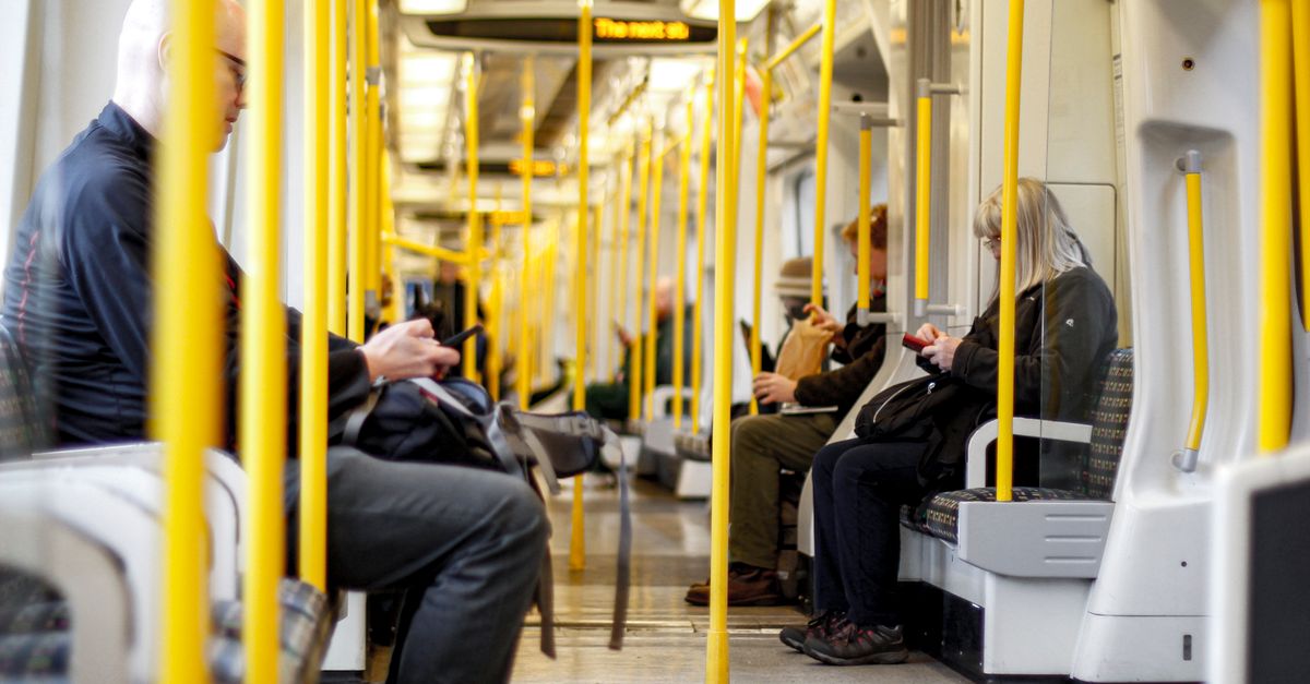 People traveling in a modern subway car, engrossed in their mobile devices.