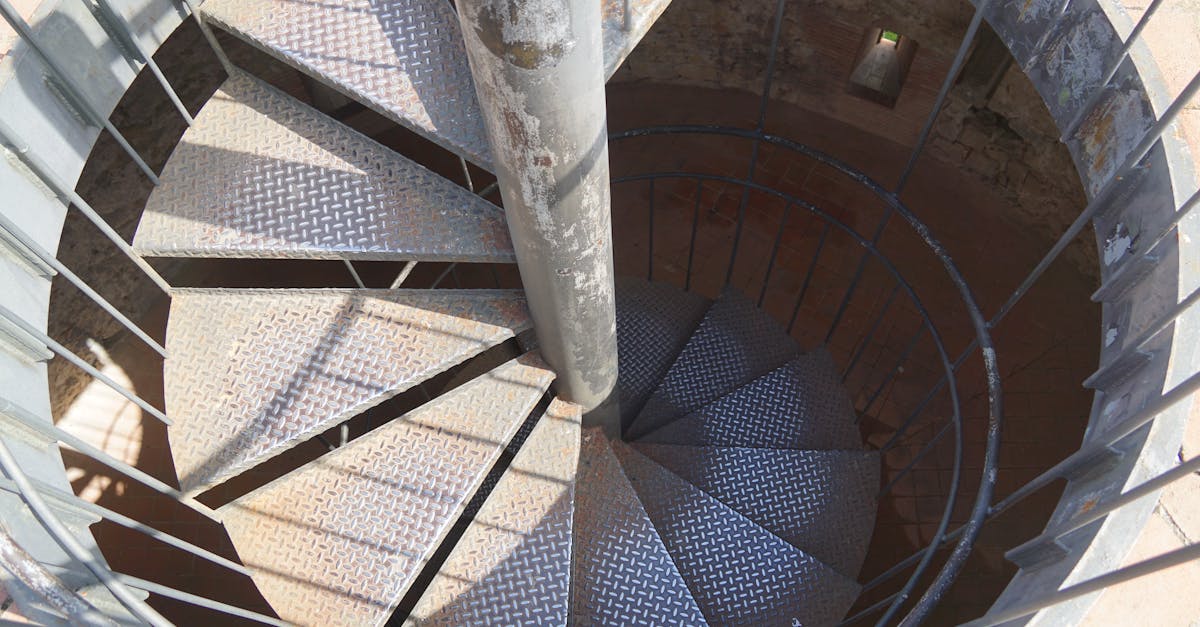 View of a spiral staircase with metal railings and checkered steps from above, showcasing industrial design.