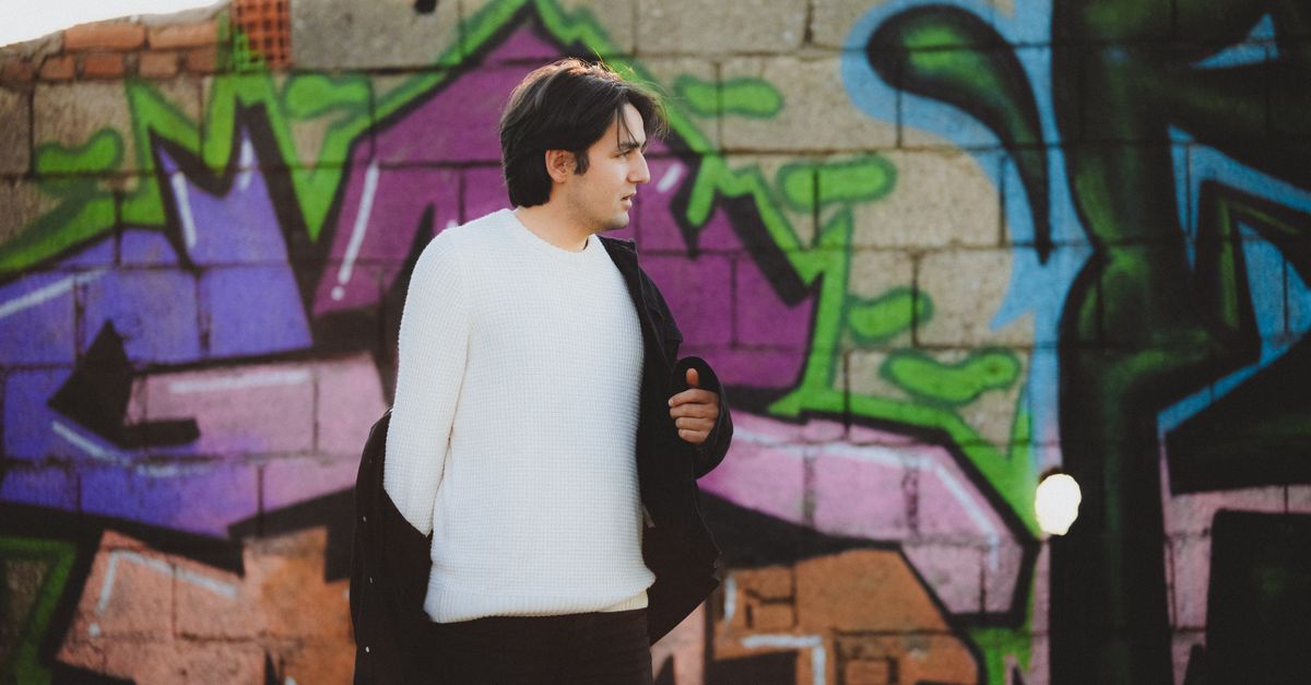 Stylish portrait of a man in a white pullover standing by a vibrant graffiti wall.