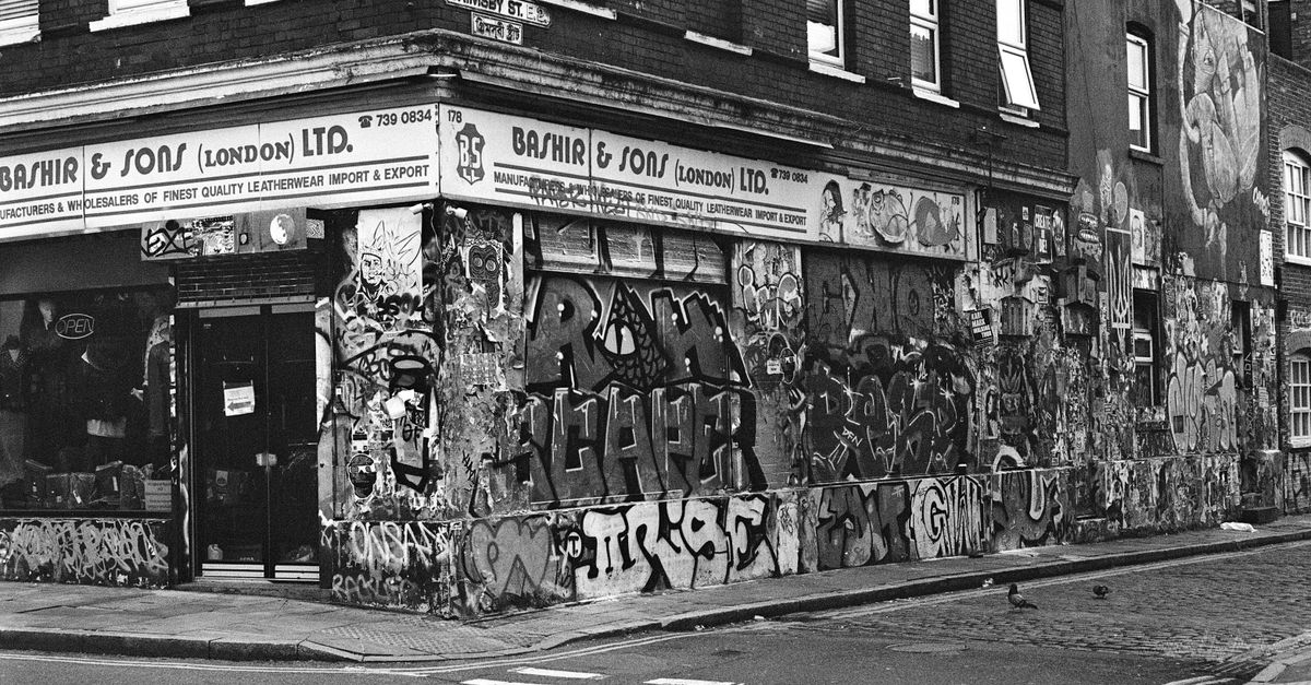 Black and white photo showcasing graffiti and street art on a London street corner with historic architecture.