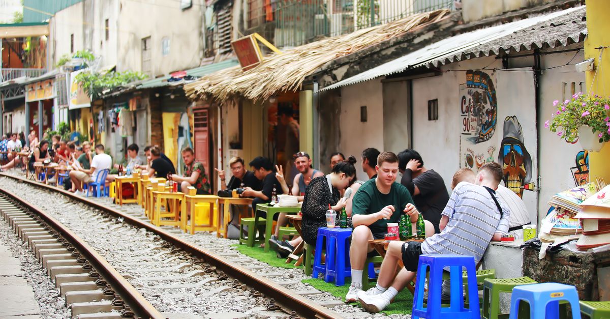 Vibrant urban scene with tourists dining at a street café beside railway tracks.