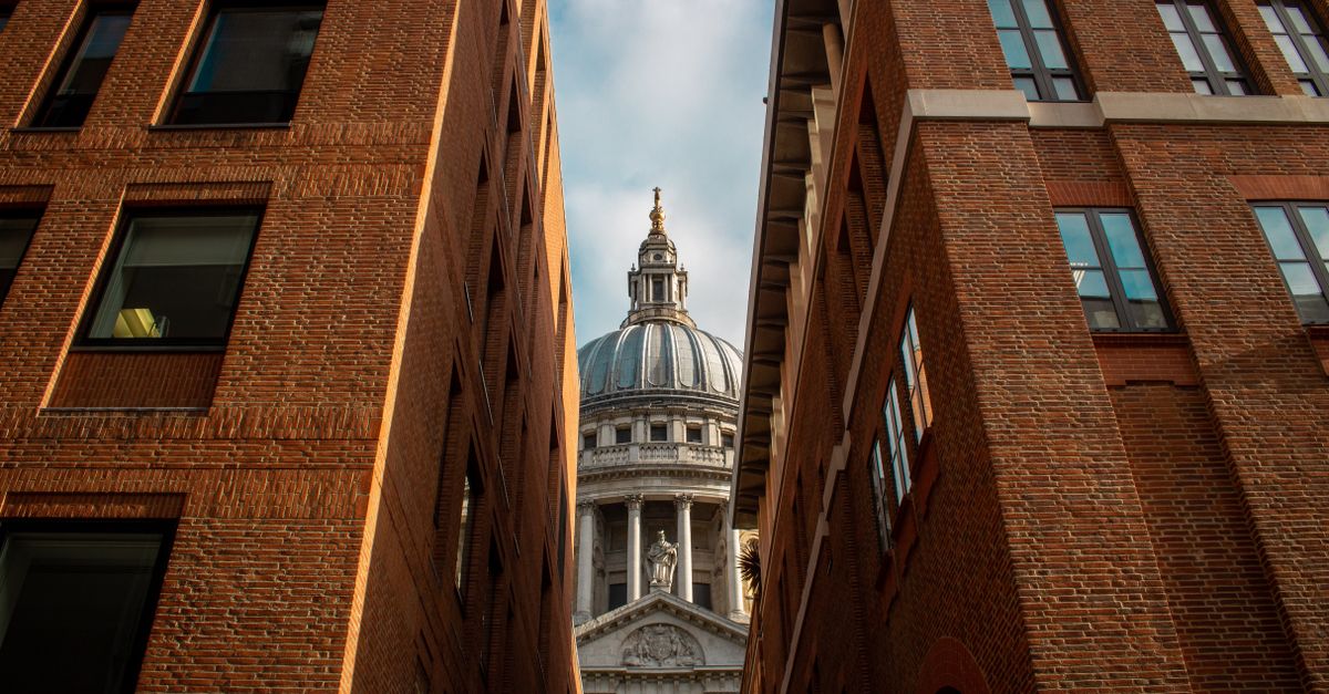 View of St Paul's Cathedral dome framed by modern brick buildings under a blue sky.