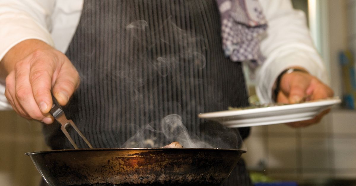A chef skillfully prepares a dish in a professional kitchen, surrounded by smoke.