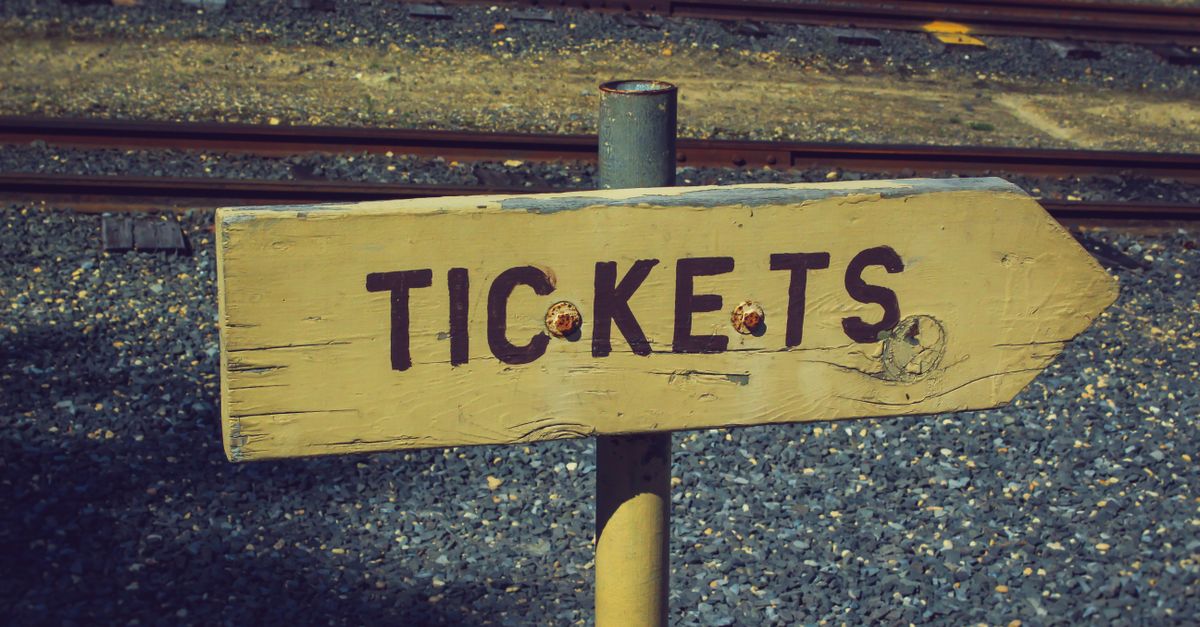 Weathered wooden ticket sign pointing towards railway tracks outdoors, vintage look.