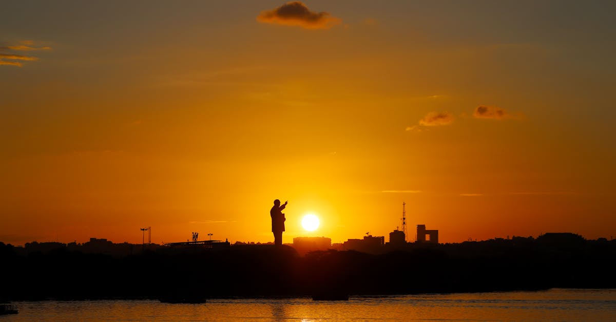 Silhouette of a city skyline with a prominent statue during a vibrant sunset.