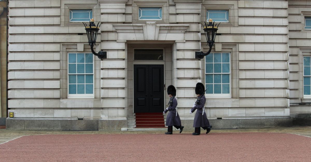 Two royal guards in traditional attire march at Buckingham Palace, London.