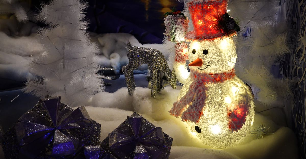 Illuminated snowman with presents and snowy trees in a Christmas display.