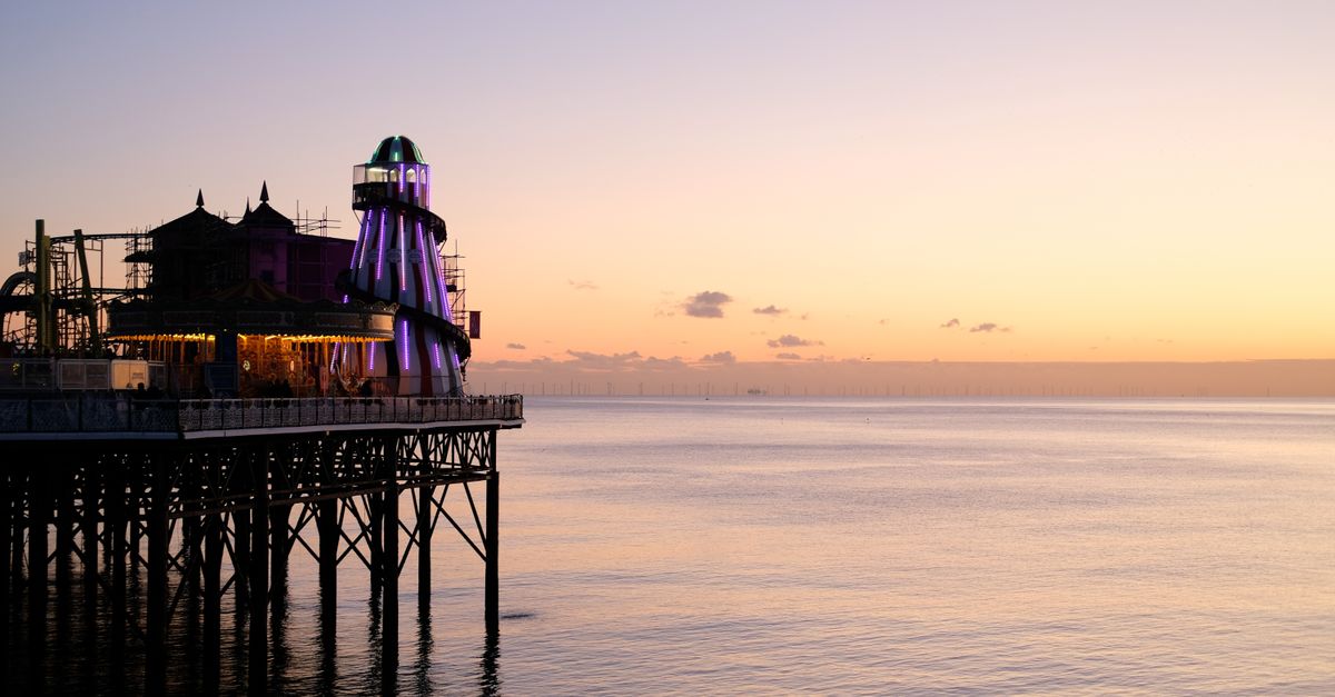 Vibrant sunset at Brighton Pier, UK, with purple lights illuminating the structure against a calm sea.