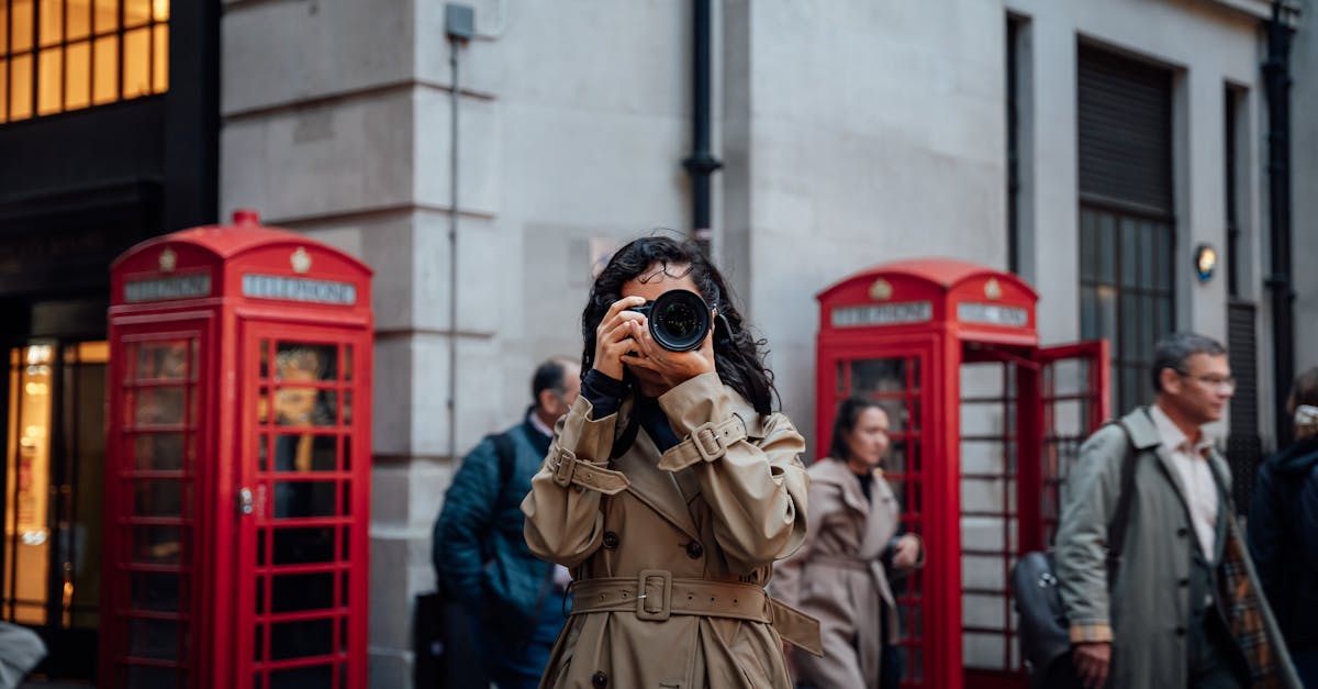 Woman photographing on a bustling London street with iconic red phone booths.