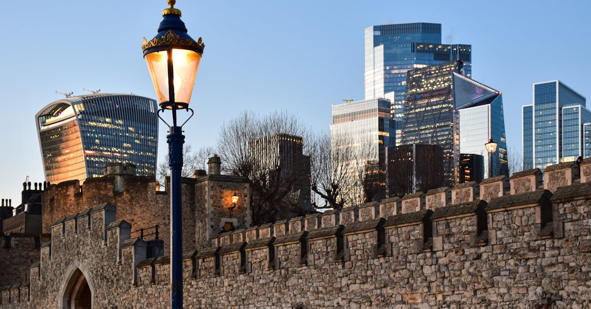 Contrasting London skyline with modern skyscrapers and historic stone wall at sunset.