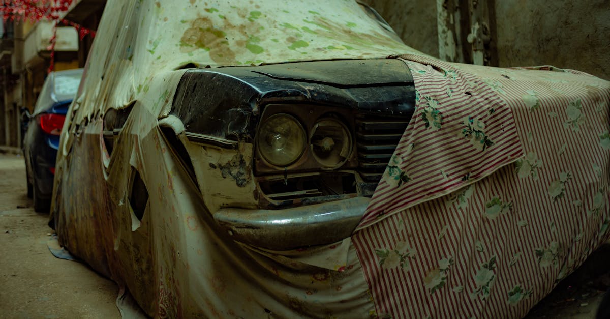 Abandoned vintage car draped in worn fabric in an urban alley, showcasing decay.