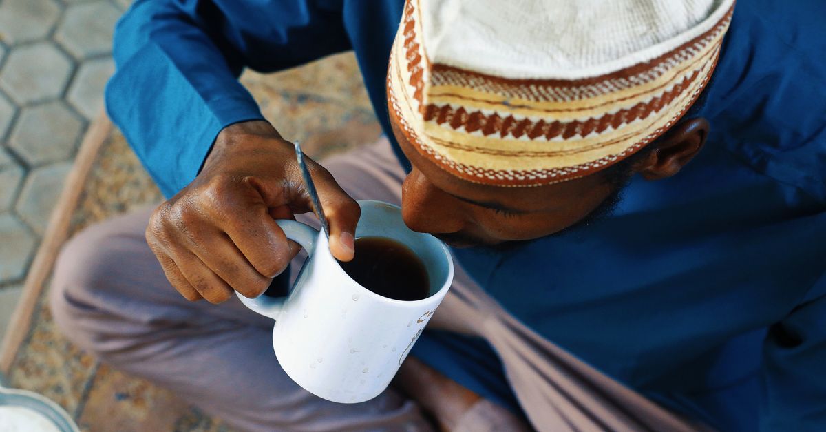African man in traditional attire enjoying a warm drink in Abuja, Nigeria, outdoors.