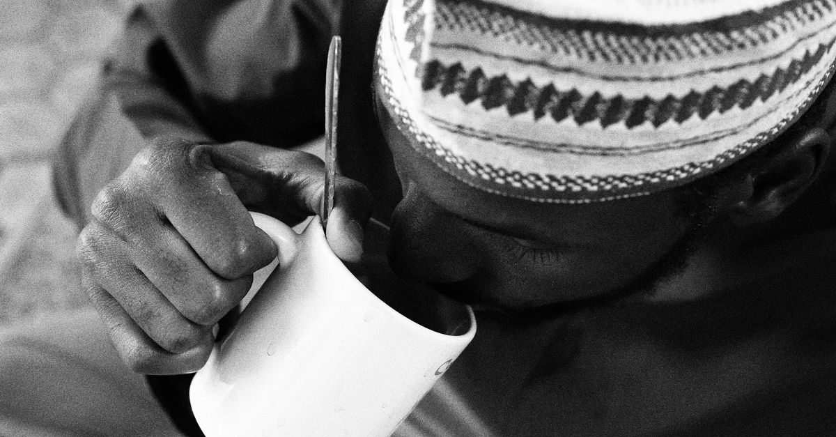 A man in traditional attire drinking from a mug, captured in black and white.