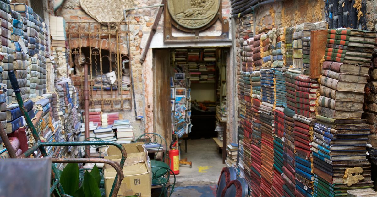 Explore a unique Venetian bookshop with colorful stacked books in a rustic alleyway.
