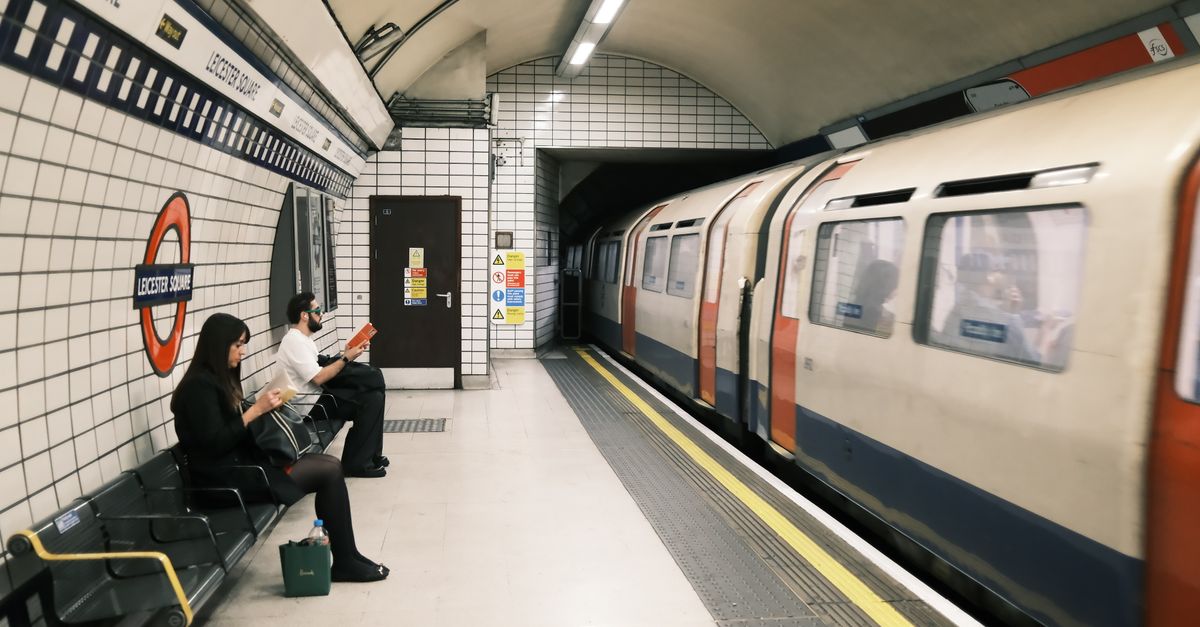 Commuters waiting at Leicester Square station with a train passing by.
