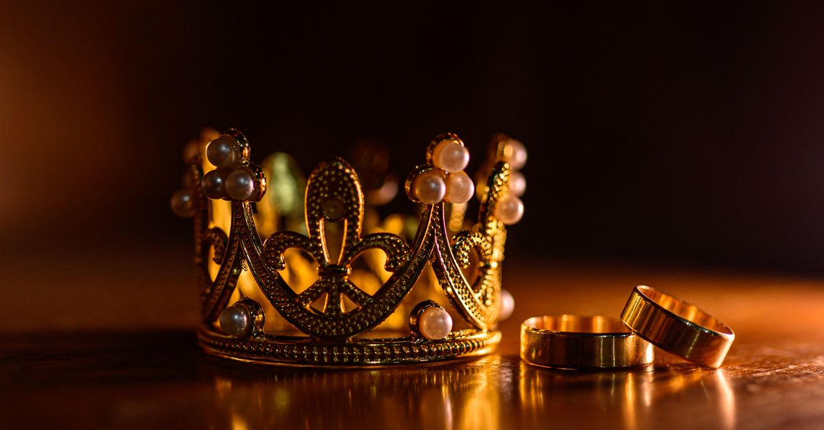 Close-up of an elegant gold crown adorned with pearls and rings on a wooden surface.