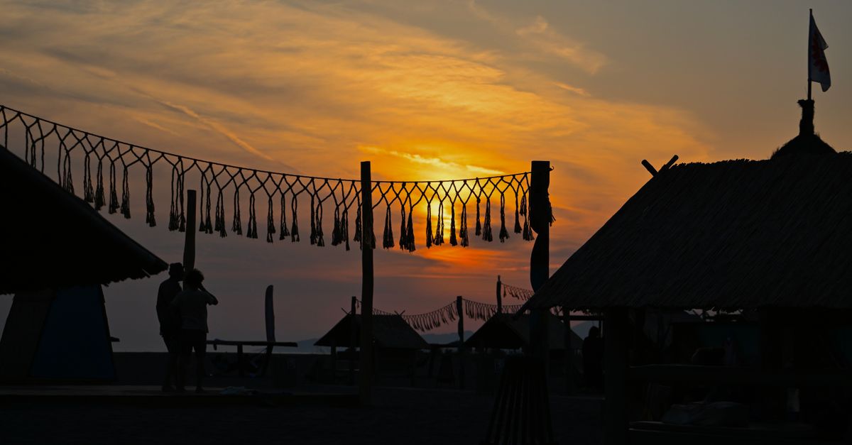 Silhouette of people enjoying a beach festival at sunset with decorative tassels.