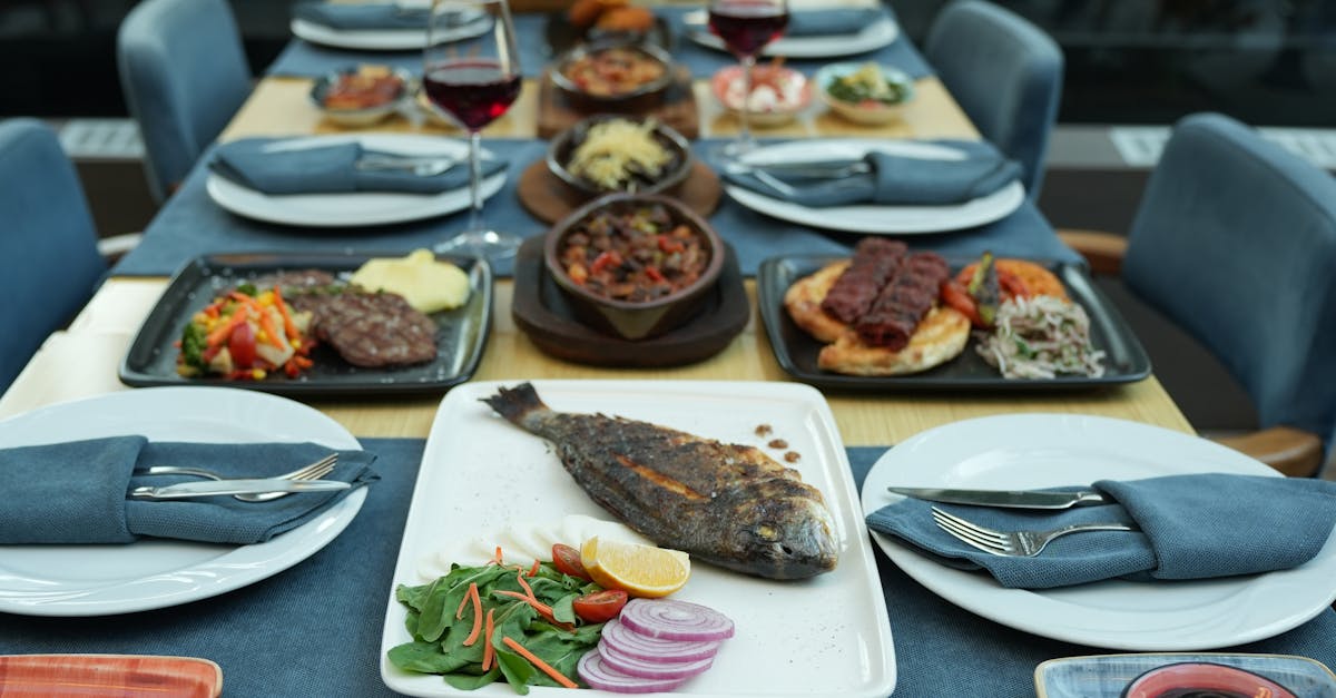 An elegant al fresco dining setup featuring grilled fish, side dishes, and red wine, perfect for a gourmet meal.
