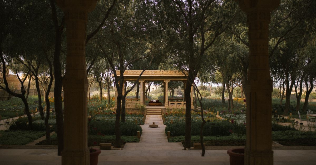 A tranquil garden scene framed by Indo-Persian style arches, showcasing lush greenery and a serene pavilion.