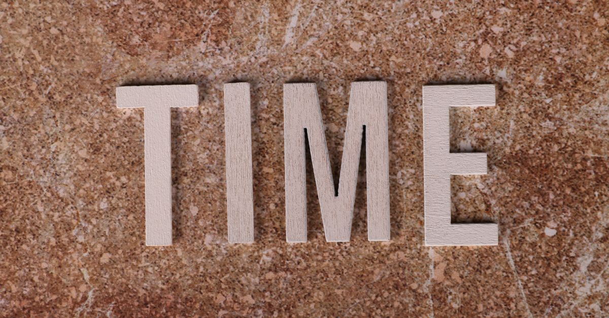 Close-up of the word 'TIME' spelled with wooden letters on a textured surface.