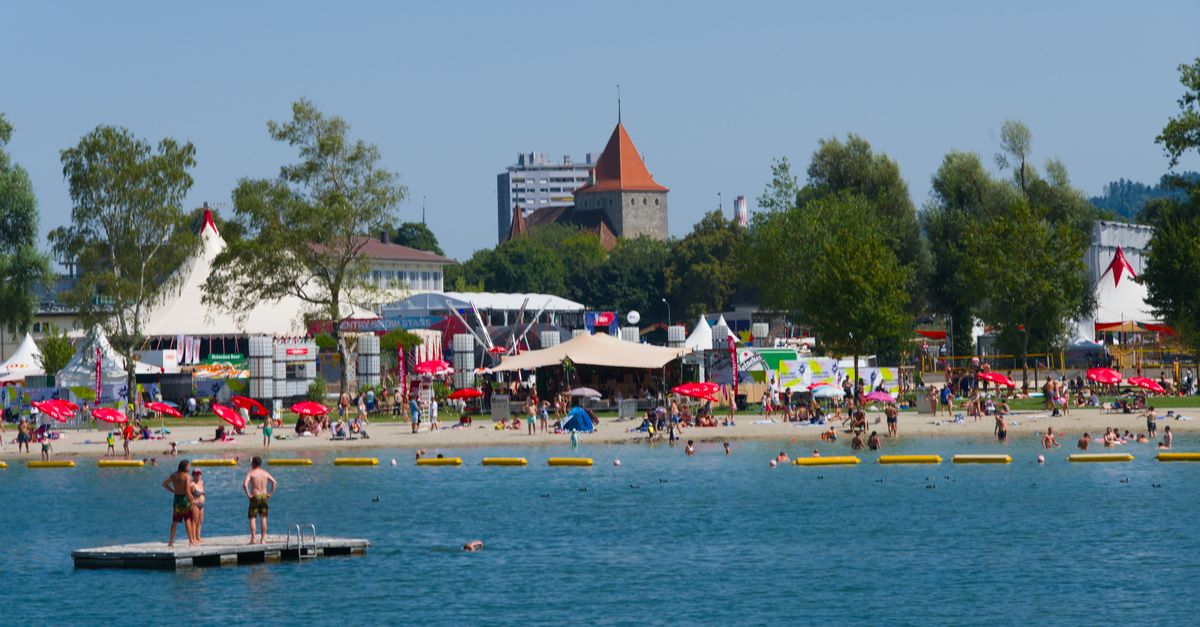 People enjoying a sunny day at Neuchâtel Lake with vibrant beach activities and festive tents.