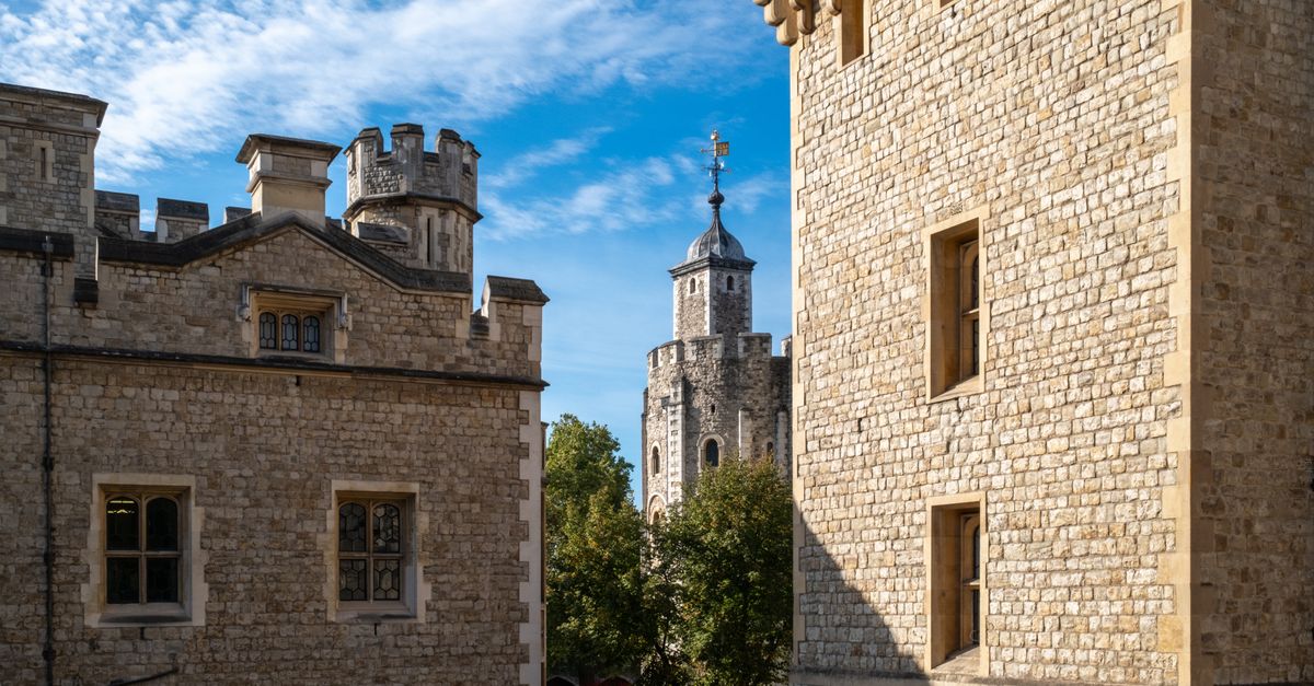 Stone towers of the historic Tower of London under a bright blue sky, England.