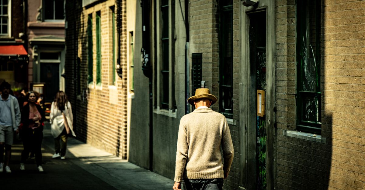 A man with a hat walks down a sunlit alleyway in Dublin, Ireland, capturing the play of light and shadow.